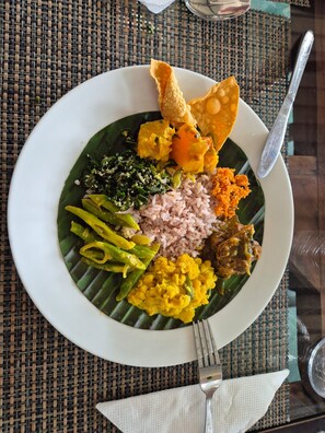 Prato de comida com arroz, legumes e um pedaço de fritura sobre um tapete de palha.