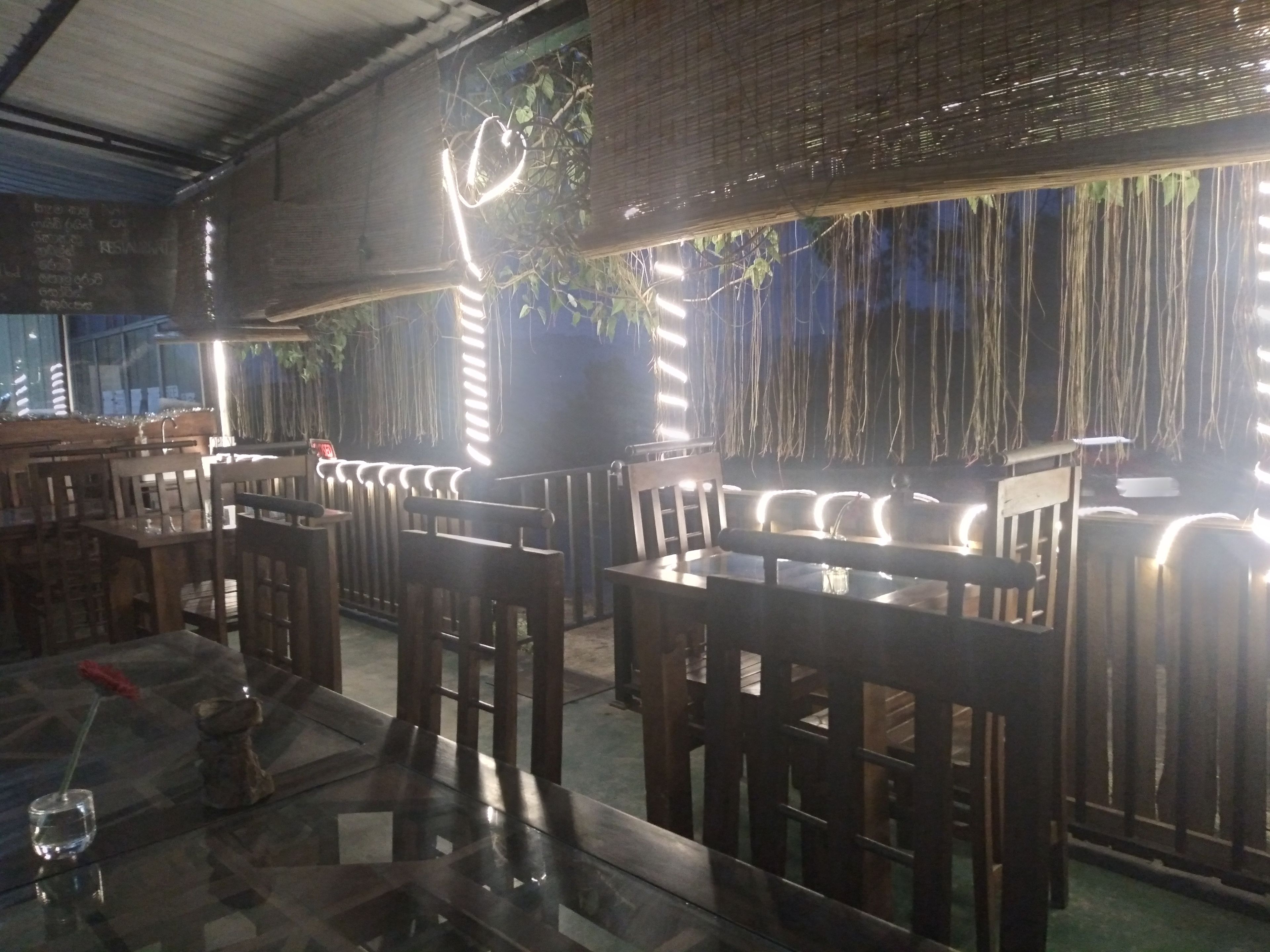 A restaurant with wooden tables and chairs, hanging plants, and string lights.