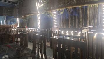 A restaurant with wooden tables and chairs, hanging plants, and string lights.