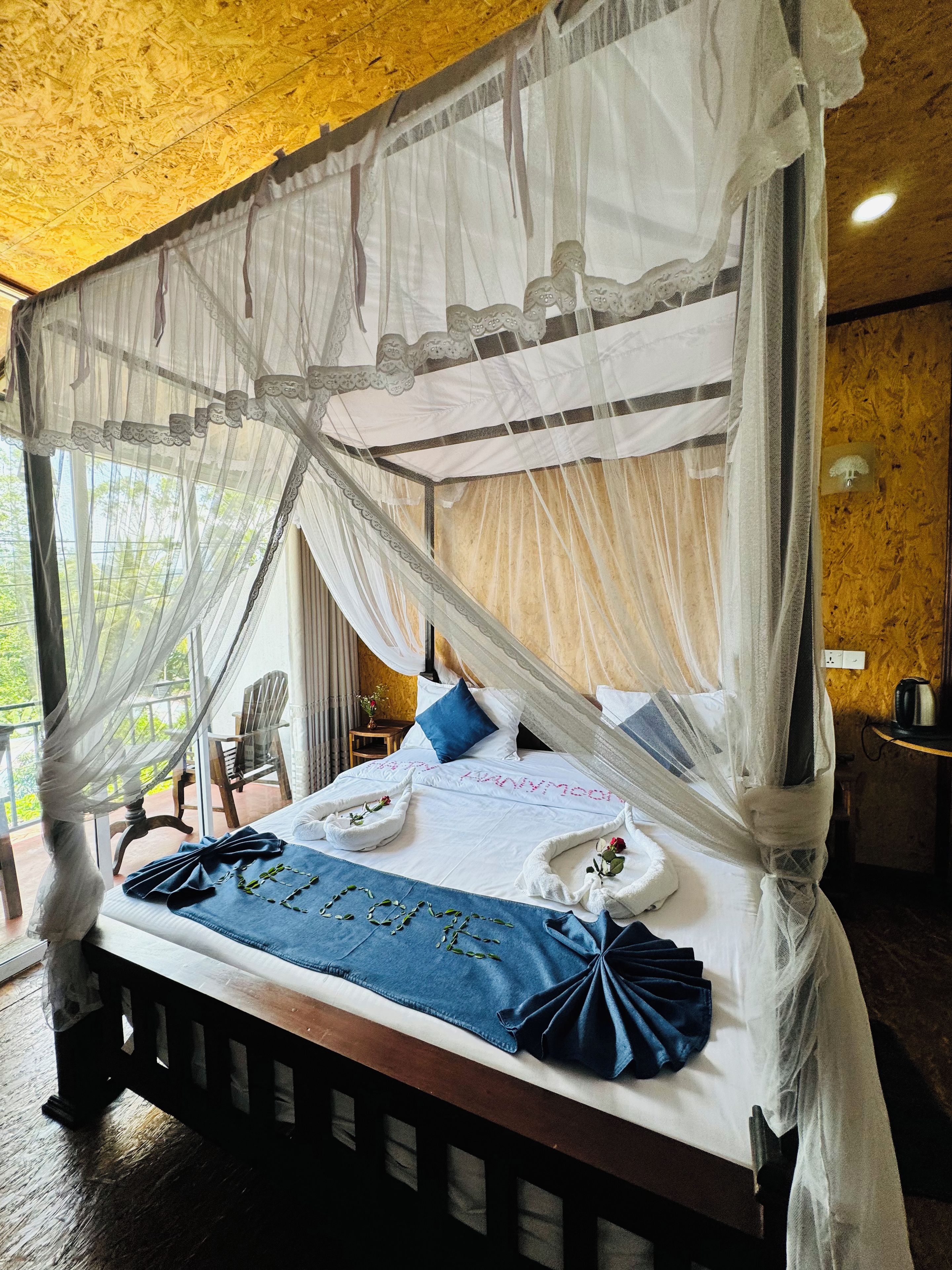 A bed with a canopy, a blue bedspread, and a welcome note.
