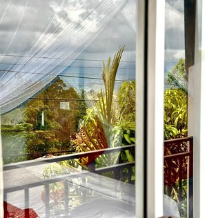 A view through a window with a mesh covering, displaying a garden with various plants and a structure in the background. - Ella Nature Life Guest & Restaurant (Ella)