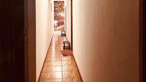 A narrow hallway with wooden flooring, a door on the left, and a bench on the right.