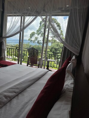 A bedroom with a large bed, a chair, and a balcony with a view of the landscape.