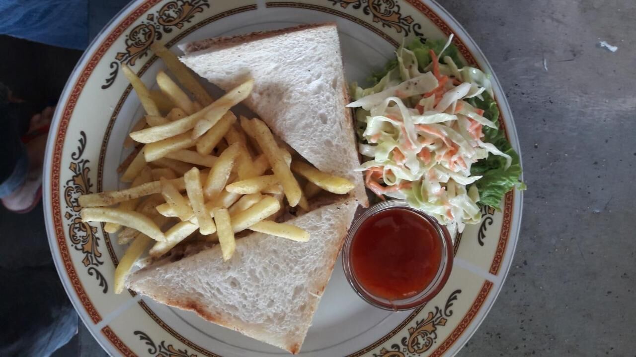 A plate with a sandwich, fries, coleslaw, and a small container of ketchup.
