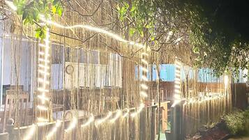 Un espace jardin agrémenté d’une clôture décorée de guirlandes lumineuses, d’un banc en bois et d’une grille métallique posée au sol.