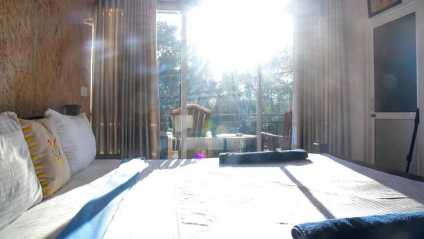 Habitación de hotel con una cama grande, una silla y una mesa junto a una ventana con vistas a árboles.
