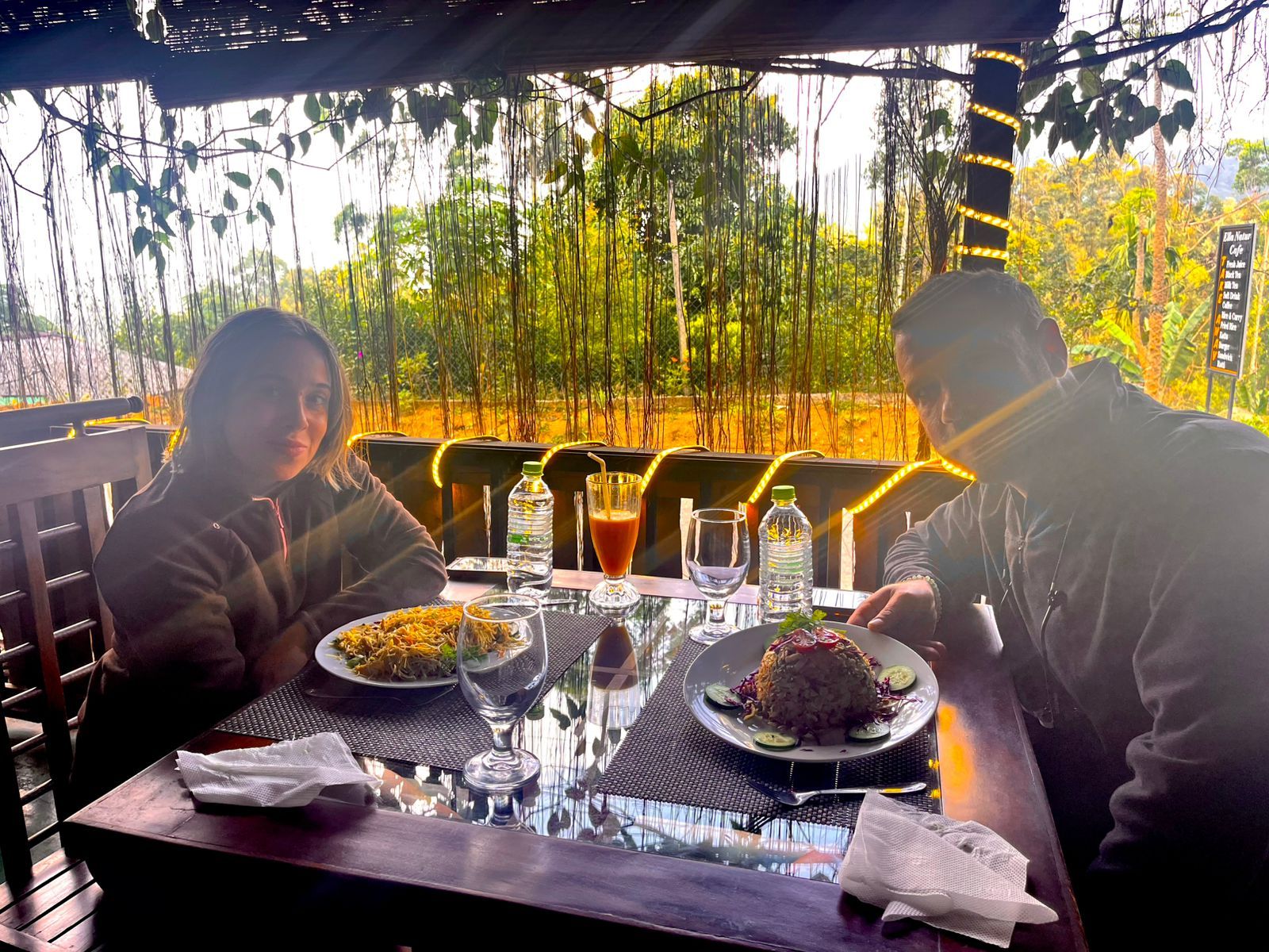 Une table à manger avec deux assiettes de nourriture, un verre de jus de fruits et une bouteille d’eau.