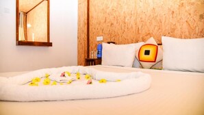 Habitación de hotel con cabecera de madera, cama con ropa blanca, mesita de noche con una botella de agua azul y un espejo en la pared.