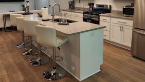 Een moderne keuken met een centraal eiland, barstoelen, roestvrijstalen apparatuur en een plafondlamp.