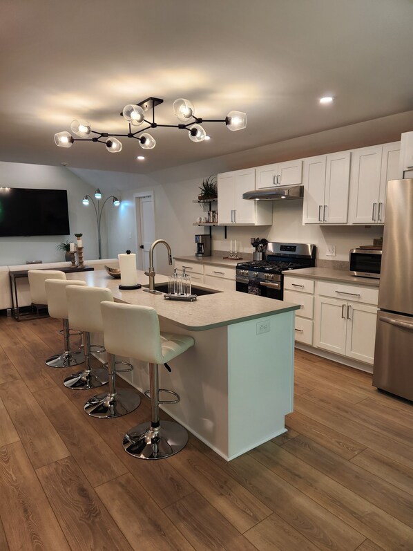 Una cocina moderna con una isla central, taburetes de bar, electrodomésticos de acero inoxidable y una lámpara colgante.