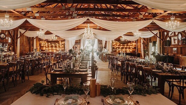 Een balzaal met lange tafels gedekt voor een formeel evenement, houten balken aan het plafond, kroonluchters en een rustieke sfeer.