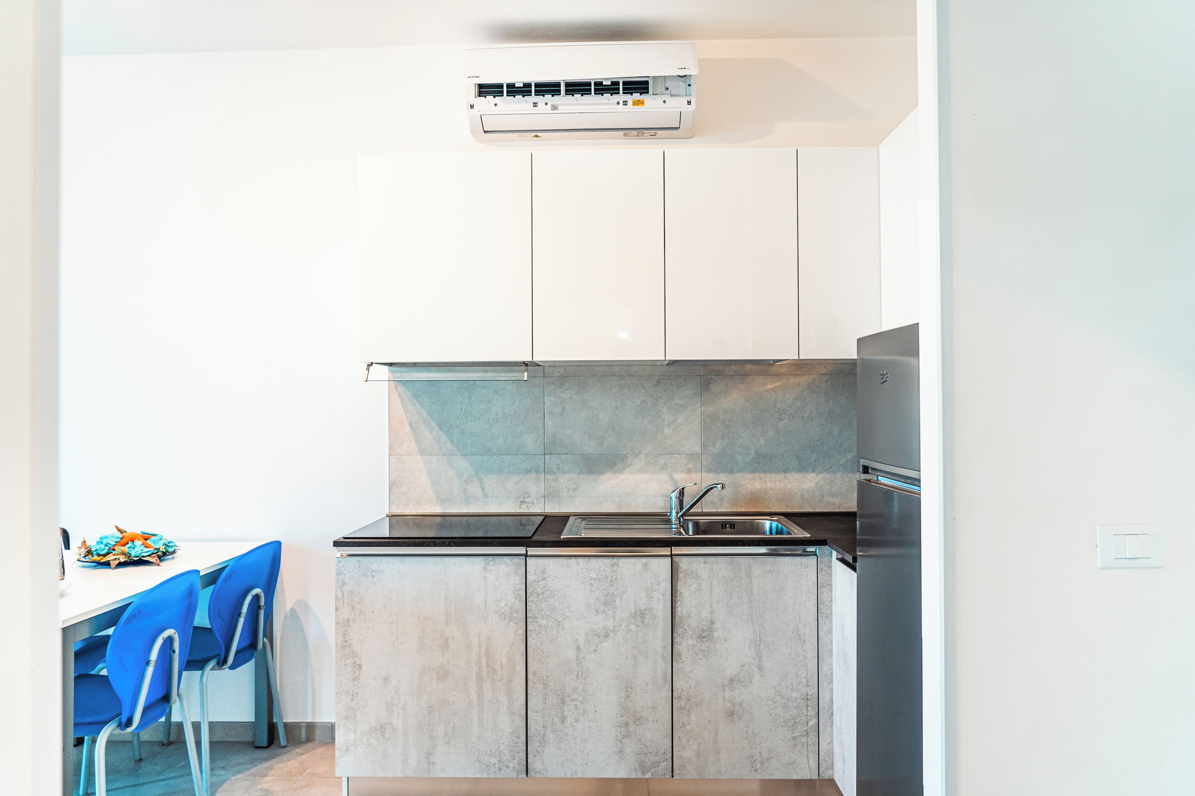 A modern kitchen with a built-in stove, sink, and an air conditioning unit above the cabinets.