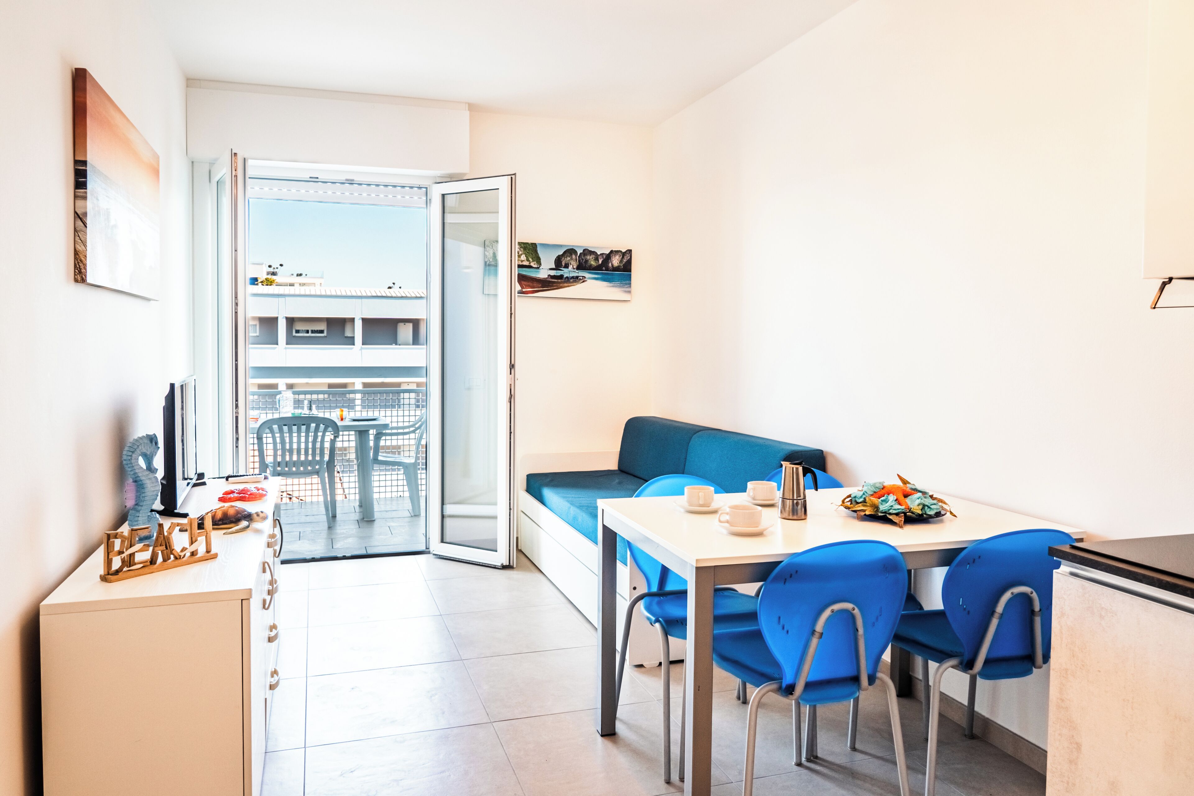 Eine moderne Wohnung mit Balkon, einem Essbereich mit blauen Stühlen und einem Sofa.