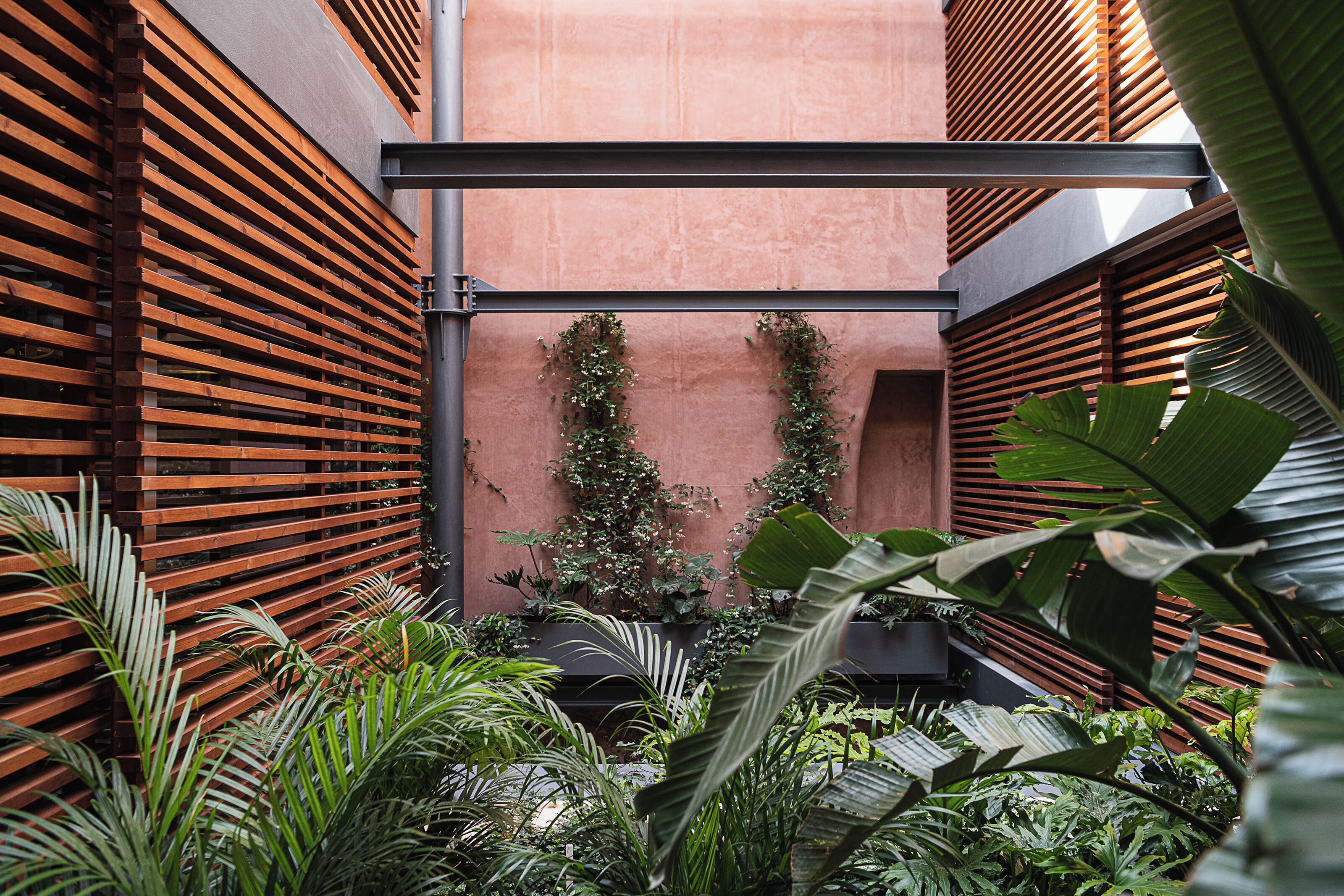 A modern outdoor space with wooden slatted walls, lush greenery, and a central vertical structure.