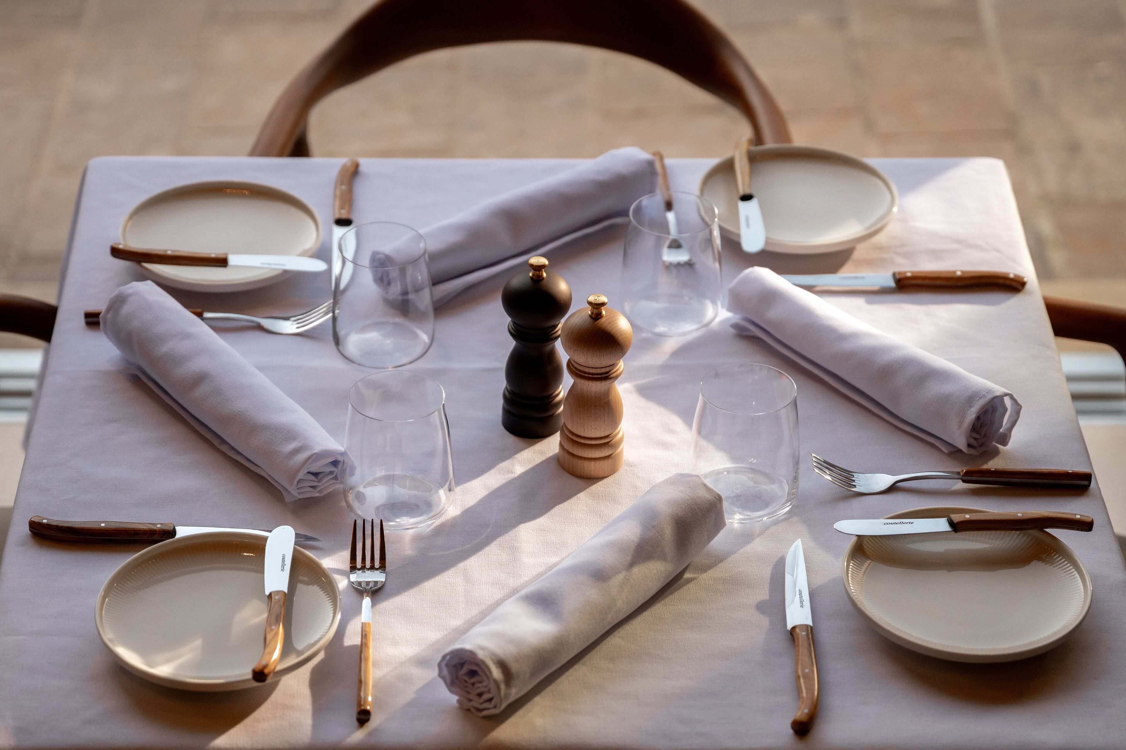 A table set for four with plates, cutlery, glasses, and a salt and pepper shaker.