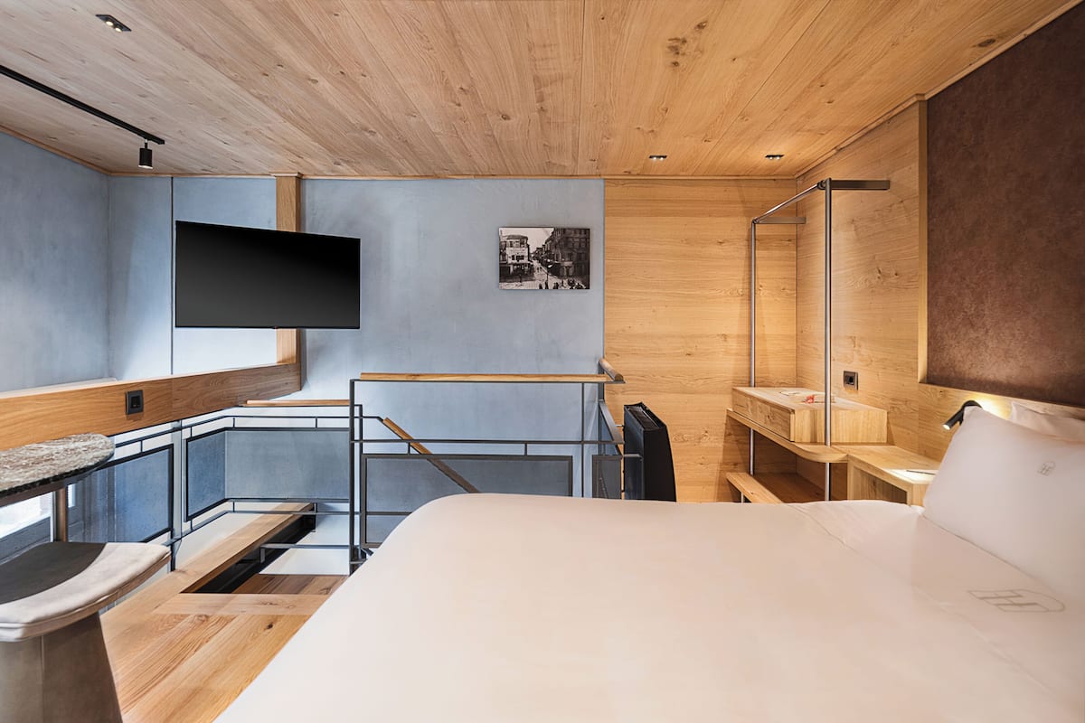 Een moderne slaapkamer met een houten plafond, een flatscreen televisie aan de muur, een bed met hoofdeinde en een klein bureau.