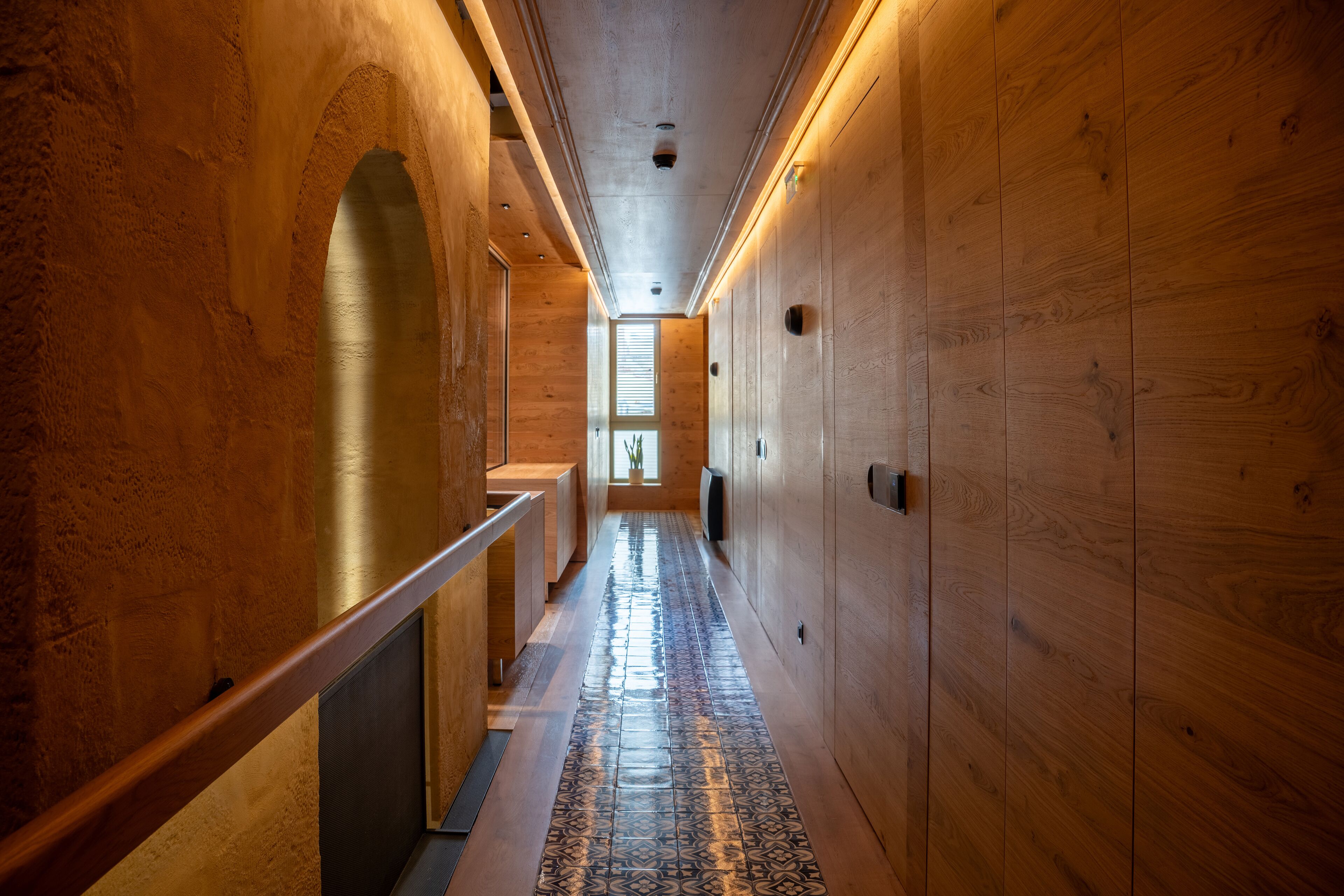 A wooden interior hallway with a patterned floor, wooden walls, and a bench along one side.