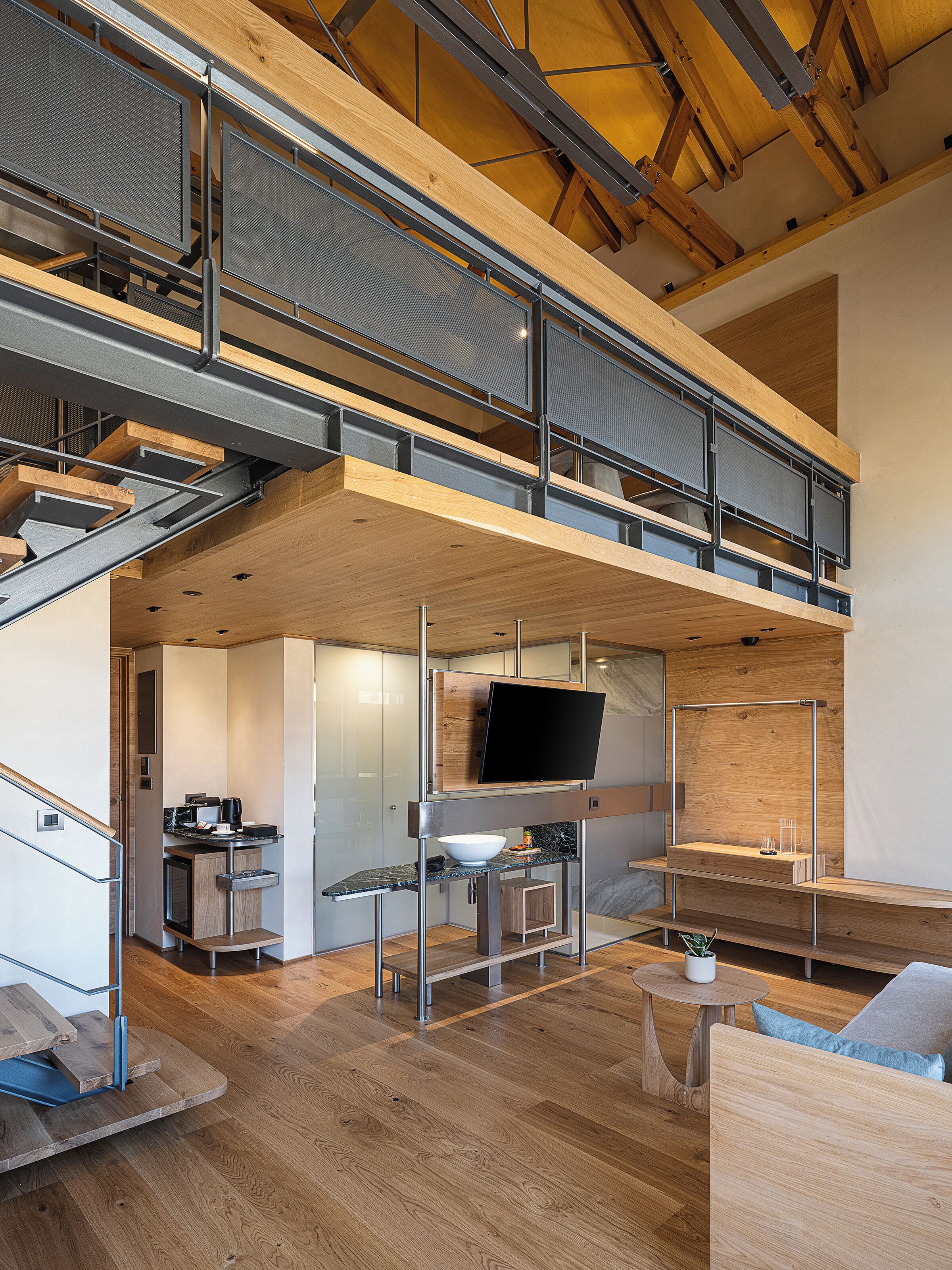 A modern loft-style apartment with a mezzanine, open kitchen, and a large TV.