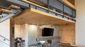 A modern loft-style apartment with a mezzanine, open kitchen, and a large TV.