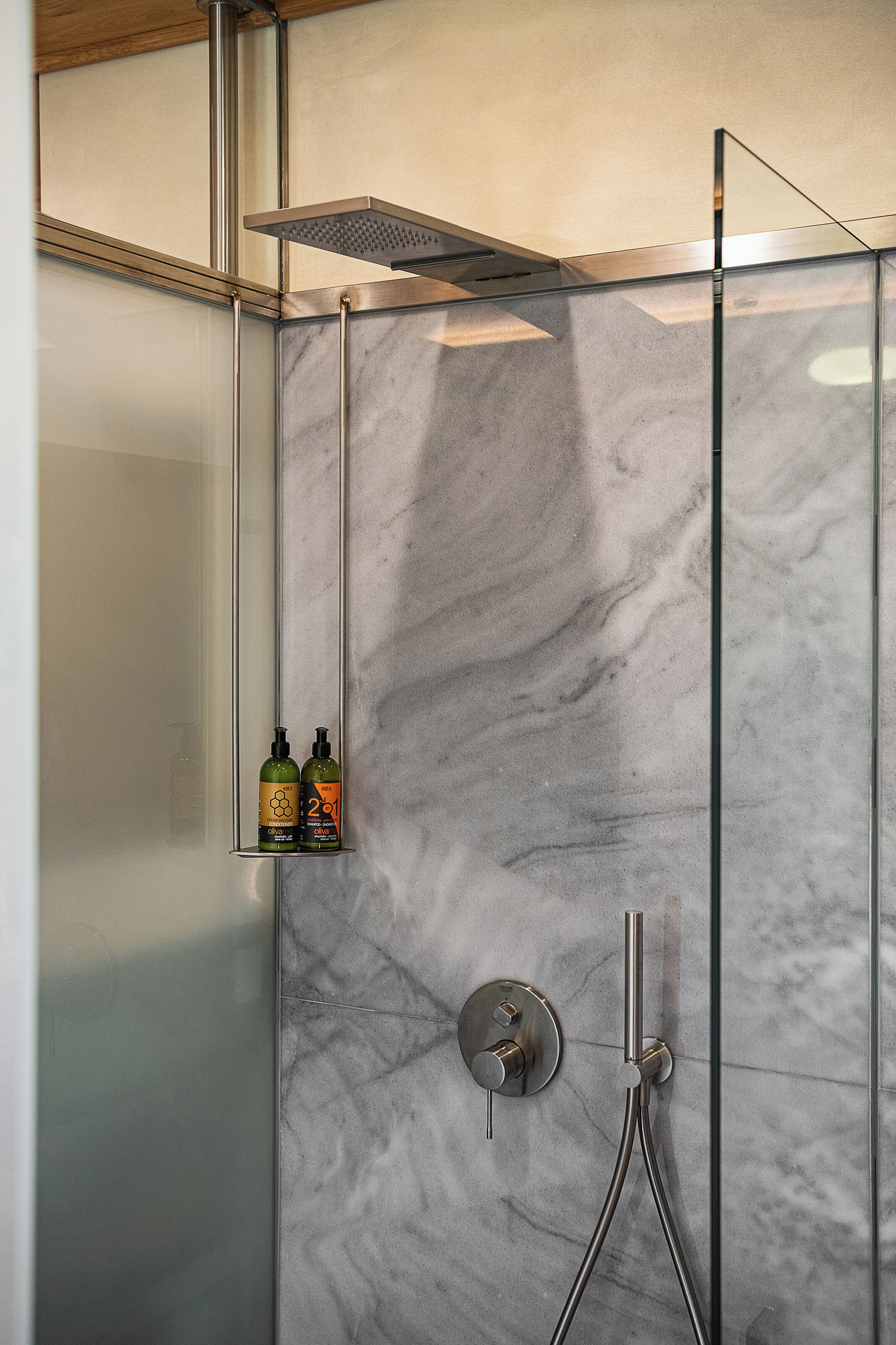 A modern shower enclosure with a glass door, a handheld showerhead, and a wall-mounted control panel.
