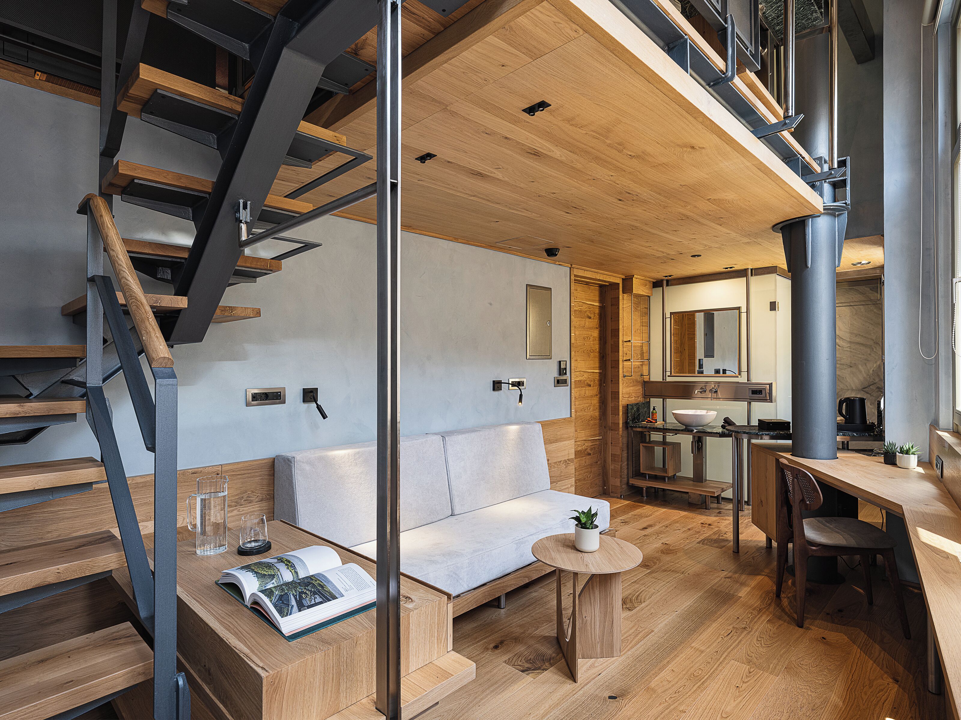 A modern interior with a staircase, a sofa, a small table with a plant, and a kitchen area.