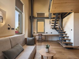Un interior moderno con una escalera de madera, un sofá con cojines, una mesita con una planta y una ventana con persianas.