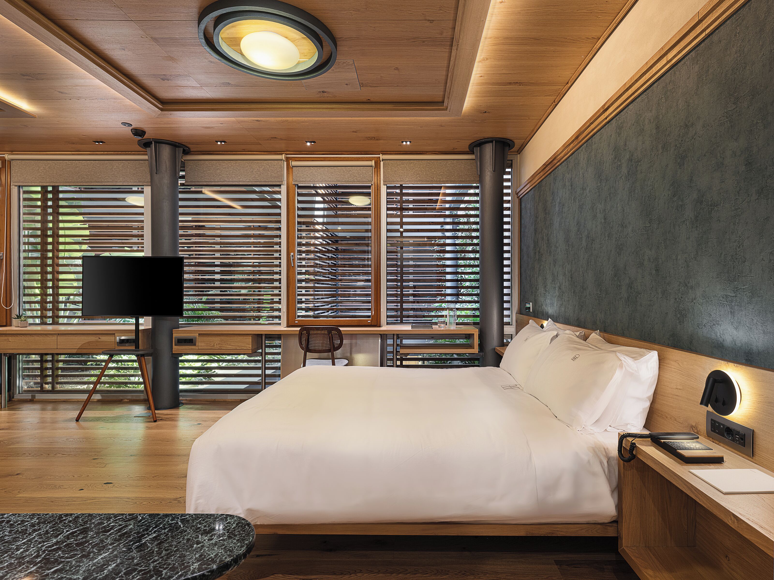 A modern bedroom with a large bed, a desk, a chair, and a TV.