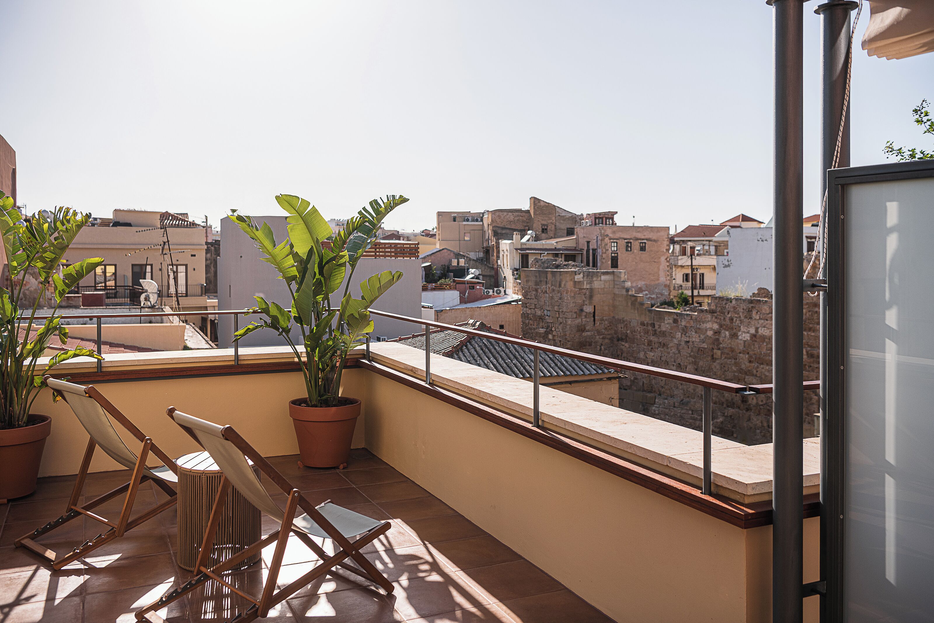 A balcony with potted plants, a chair, and a view of the cityscape.