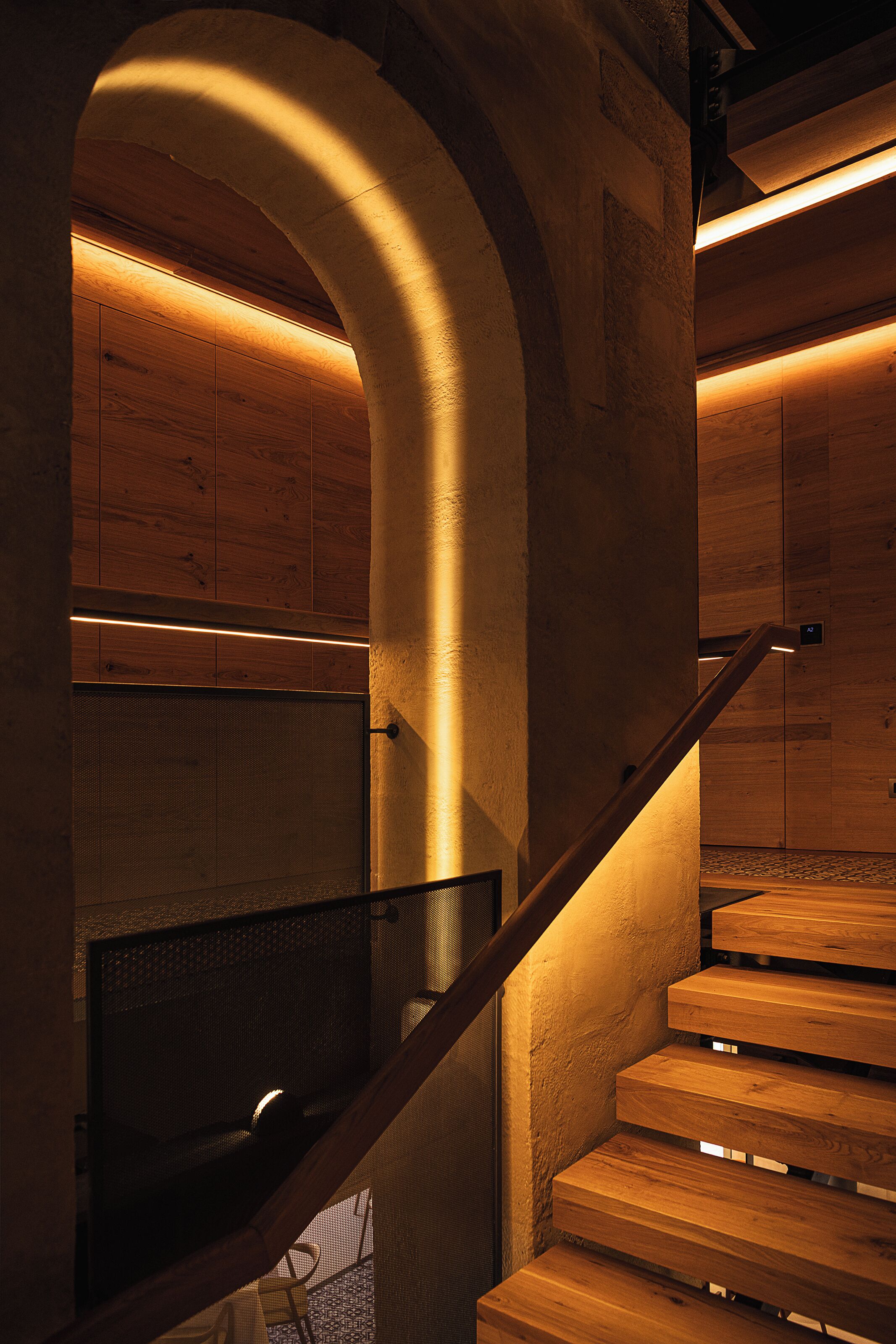 Un escalier en bois avec une rampe métallique, menant à une pièce aux murs lambrissés et dotée d’un moustiquaire.