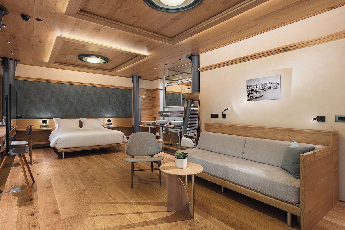 Een moderne hotelkamer met een houten plafond, een bed, een bank, een bureau en een stoel.