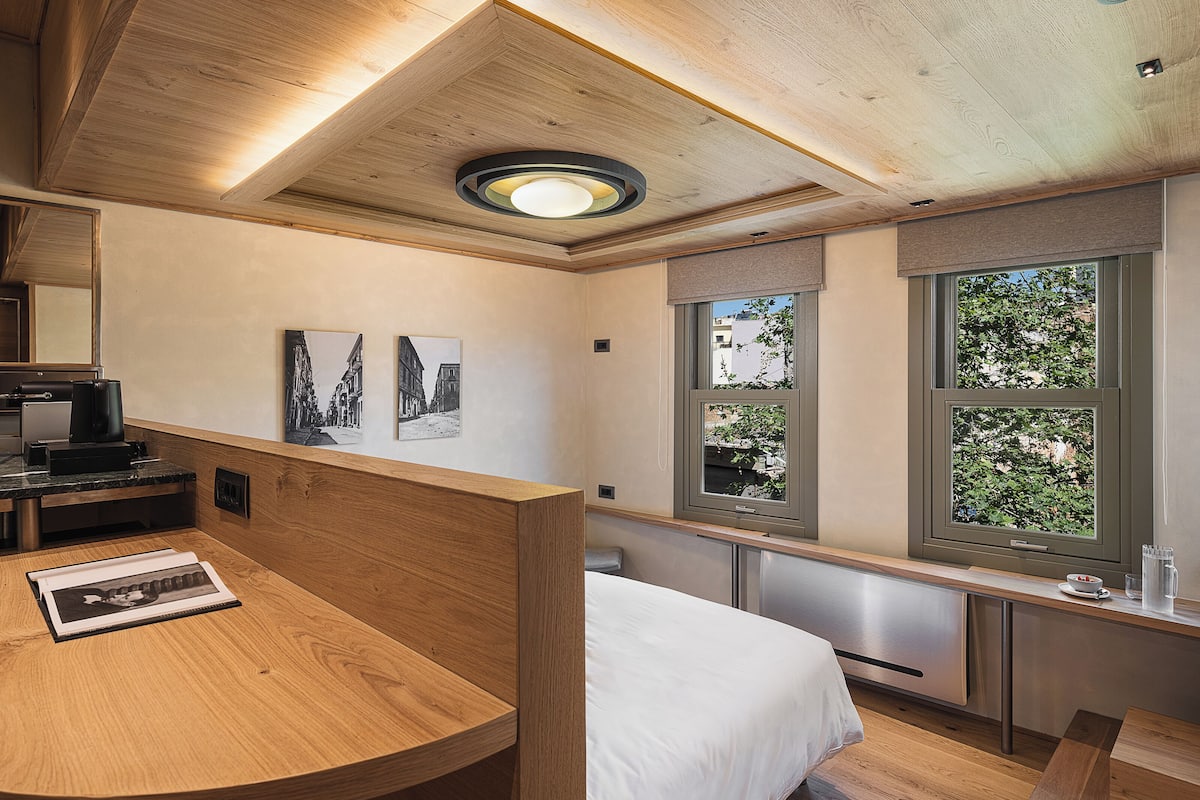 Een moderne hotelkamer met een houten plafond, een bed, een bureau met een laptop en twee ingelijste foto’s aan de muur.