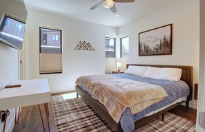 Quarto com cama, escrivaninha e televisão na parede.