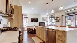 Une cuisine moderne avec des meubles en bois, des appareils en acier inoxydable et des luminaires suspendus.