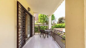 A covered balcony with a tiled floor, a table and chairs, and a decorative metal fence.