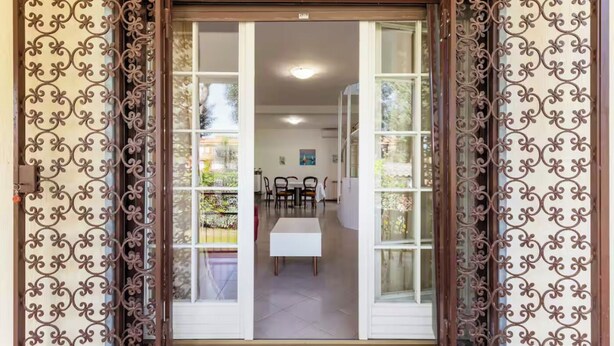 A sliding glass door with intricate metalwork, leading to an interior space with a dining area and a view of the outdoors.
