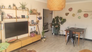 A living room with a TV, wooden entertainment unit, dining table, chairs, and a large potted plant. - Well-decorated family home, 2 steps from the bike path. (Agde)