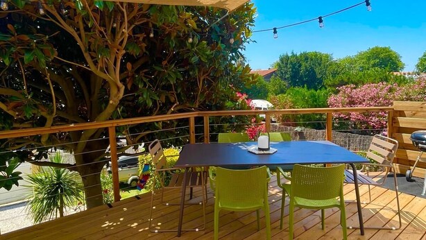An outdoor patio with a table and chairs, surrounded by a wooden deck and a large shade sail. - Well-decorated family home, 2 steps from the bike path. (Agde)