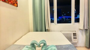 Une chambre d’hôtel avec un lit, une fenêtre avec des rideaux, un climatiseur fixé au mur et un tableau.