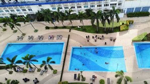 Un vaste espace extérieur avec une grande piscine et deux autres piscines séparées, entouré de chaises longues et de palmiers.