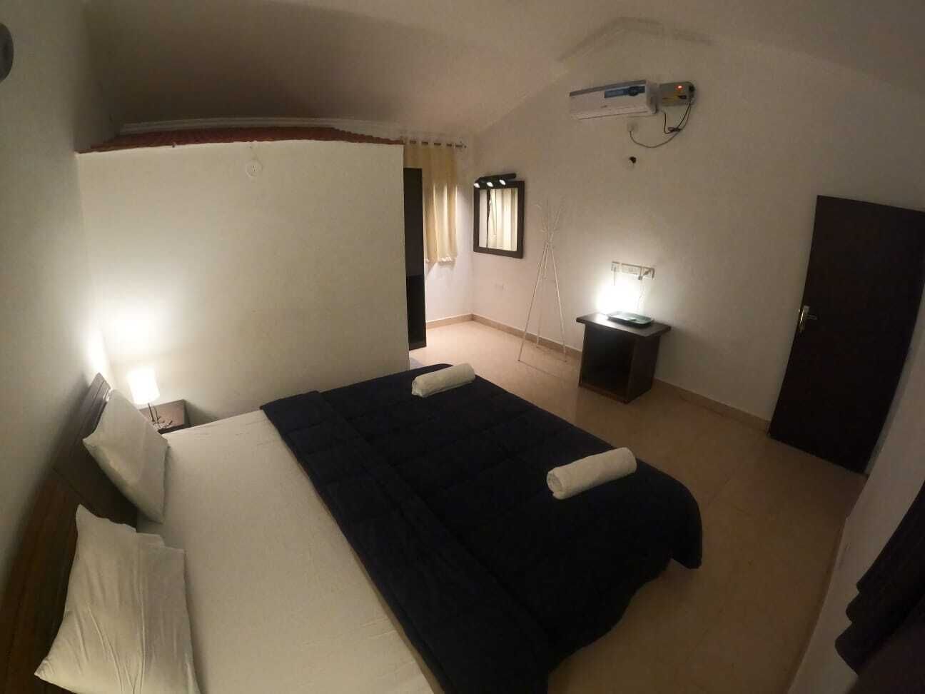 A bedroom with a bed, bedside tables, a desk, a chair, a wardrobe, and a window with curtains.
