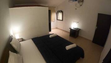 A bedroom with a bed, bedside tables, a desk, a chair, a wardrobe, and a window with curtains.