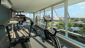 Une salle de sport équipée de matériel d’exercice et dotée de grandes fenêtres offrant une vue sur la ville.