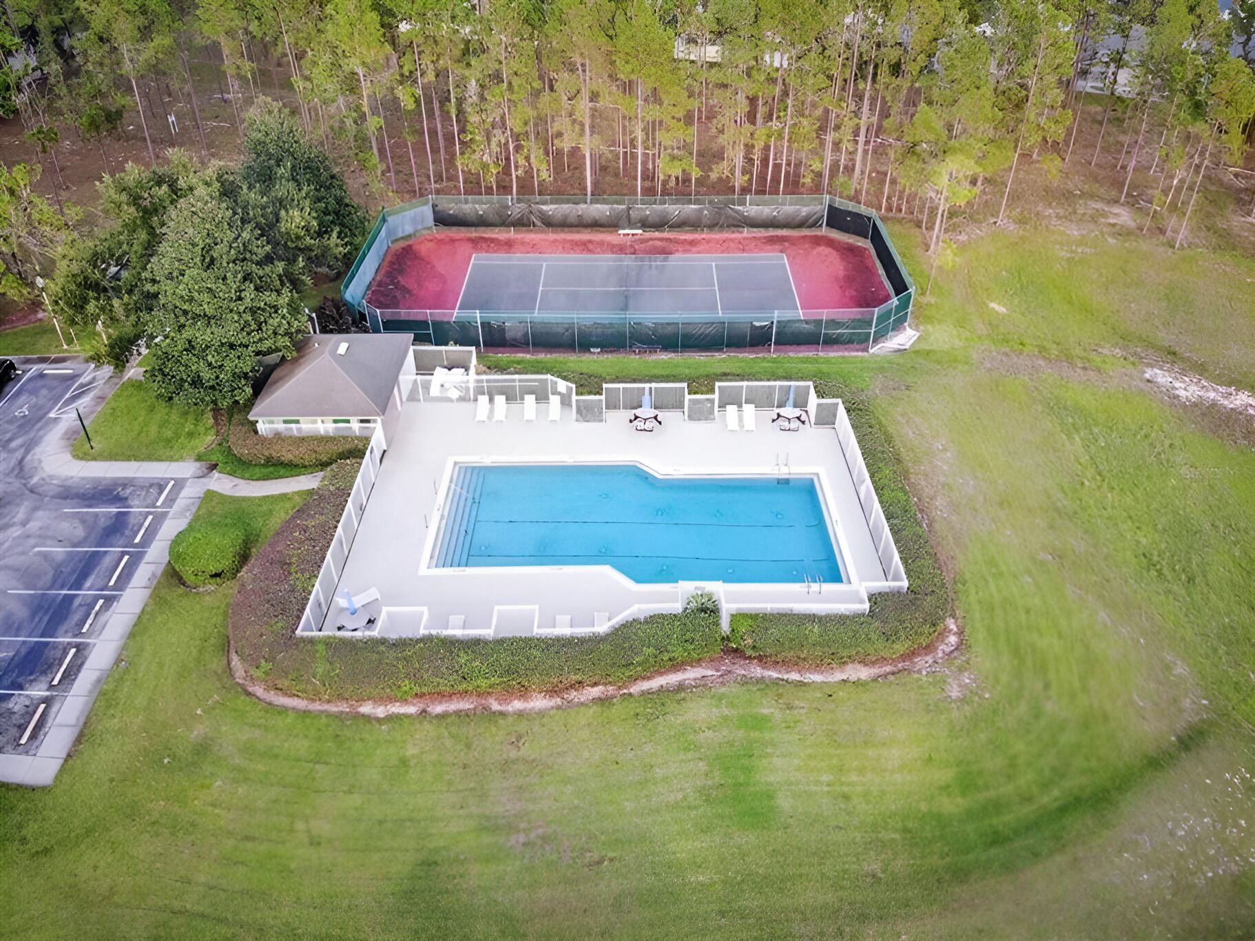 En vy över en fastighet från ovan, där man kan se en swimmingpool, en tennisbana och ett takförsett område med sittplatser.