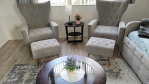 Ein modernes Wohnzimmer mit einem runden Glastisch, zwei Sesseln, einem Sofa und einem kleinen Beistelltisch mit einer Pflanze.