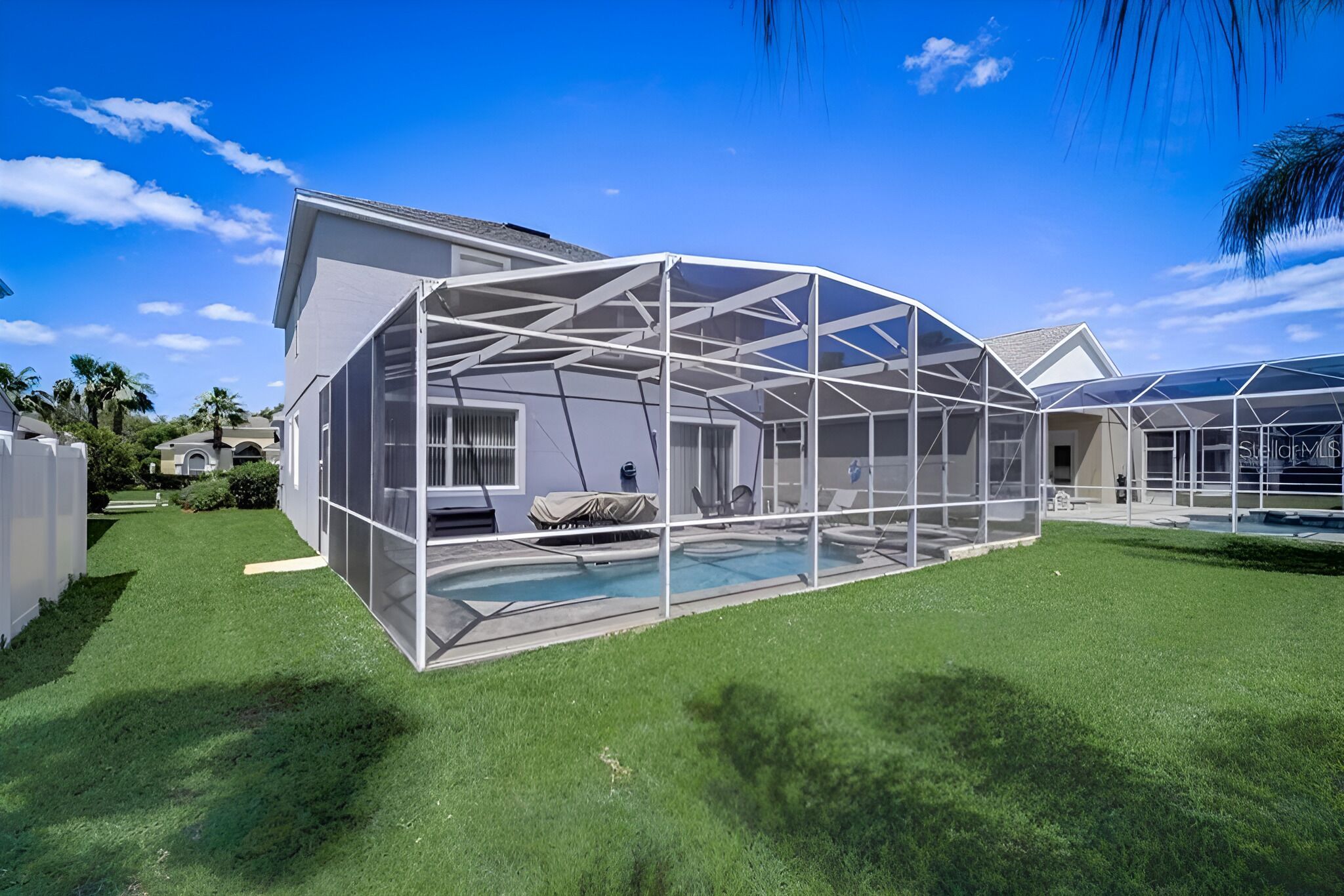Une maison moderne dotée d’un grand patio entièrement vitré, d’une piscine et d’une pelouse bien entretenue.