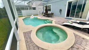 Ein überdachter Außenpool mit Whirlpool, eine Terrassenfläche mit Tisch und Stühlen sowie ein Blick auf ein Haus im Hintergrund.