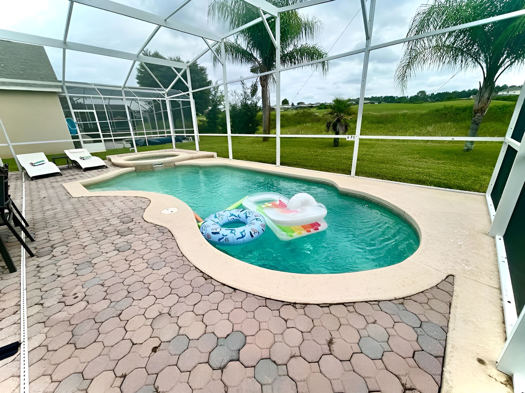 A swimming pool with hexagonal tiles, lounge chairs, and a covered area with a glass roof.