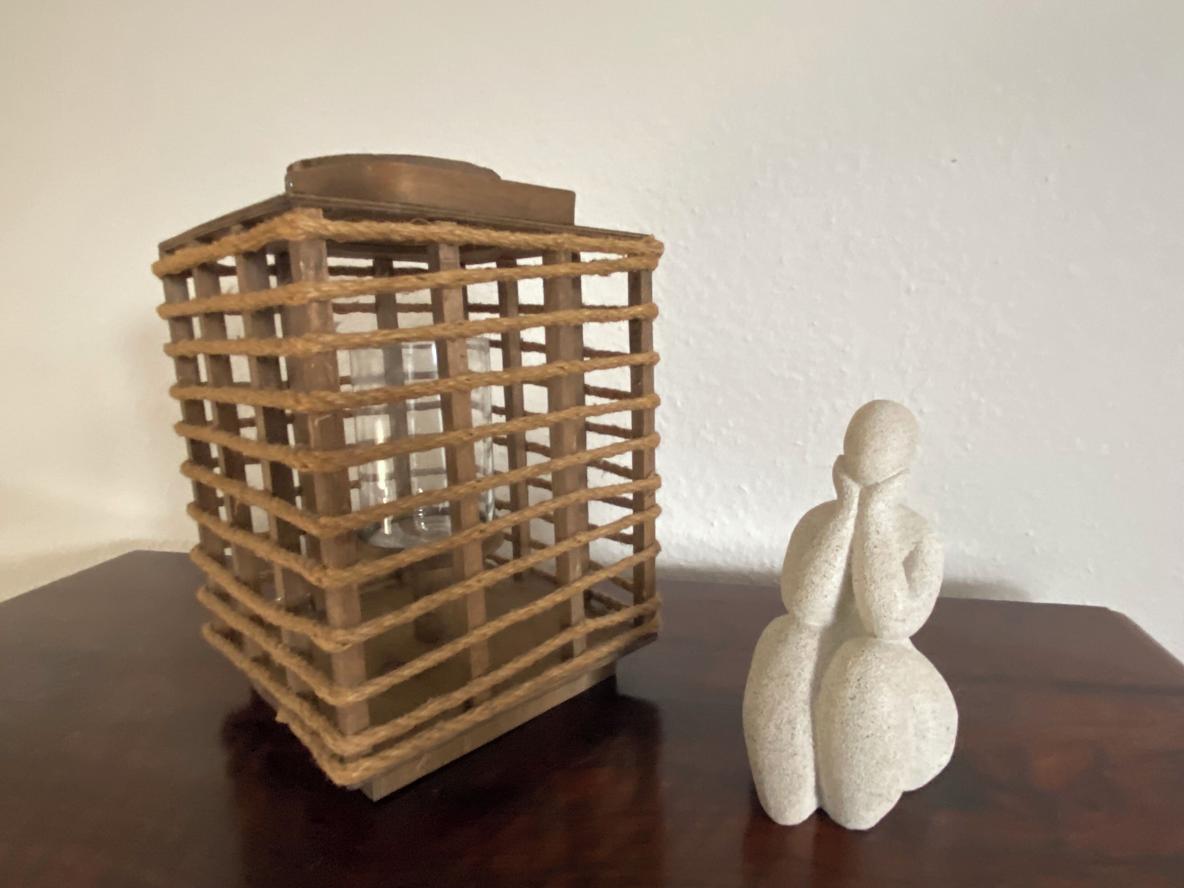 Eine hölzerne Laterne mit Gittermuster und einer kleinen Figur daneben.