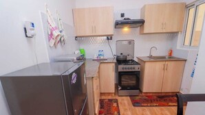 Une cuisine de taille réduite, équipée d’un réfrigérateur, d’une cuisinière et de meubles de rangement en bois.