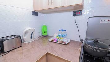 A compact kitchen with a toaster, kettle, green bottle, and water bottles on the counter.